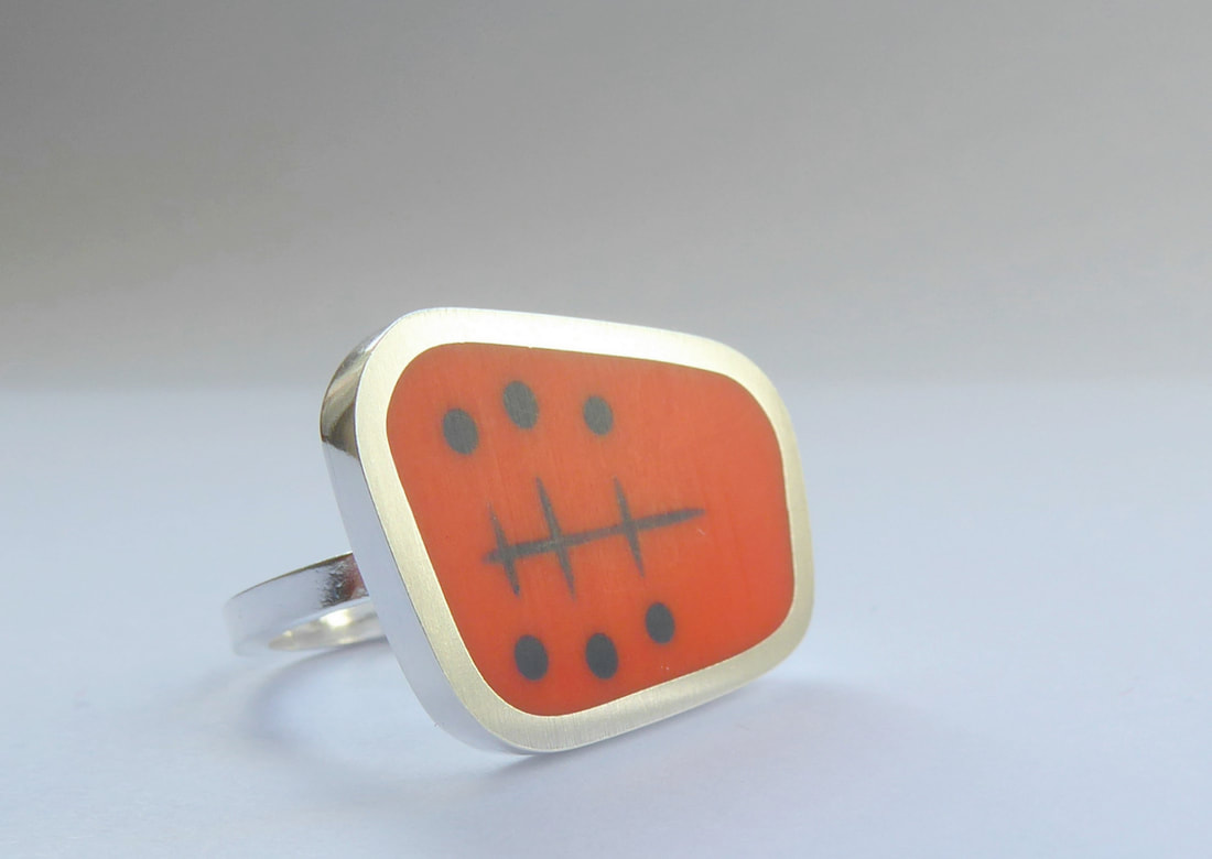 Picture of a geometric silver statement ring with orange resin centre and atomic fifties design in blue