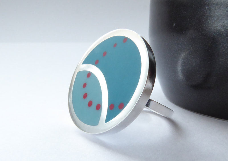 round silver cocktail ring in teal blue resin with a curved design in orange dots